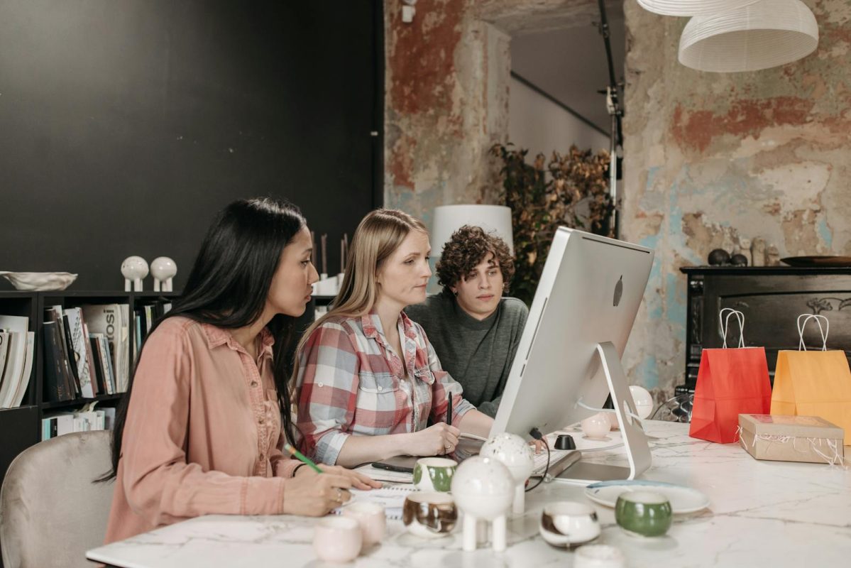 A diverse team of three adults working together on a computer in a modern office.