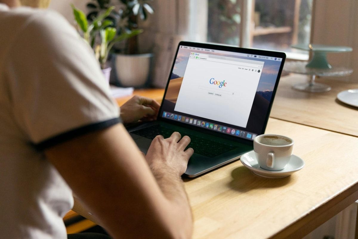 Osoba radi na laptopu za stolom pored šolje kafe, simbolično predstavljajući tehničku optimizaciju sajta i strategije kako smanjiti TTFB za brže učitavanje stranica.