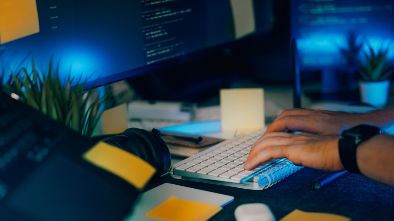 Hands typing on a keyboard with computer screens.